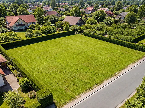 Grundstück unbebautes Baugrundstück mit Rasenfläche, Hecken, Straßenanbindung und Wohnhäusern im Umfeld