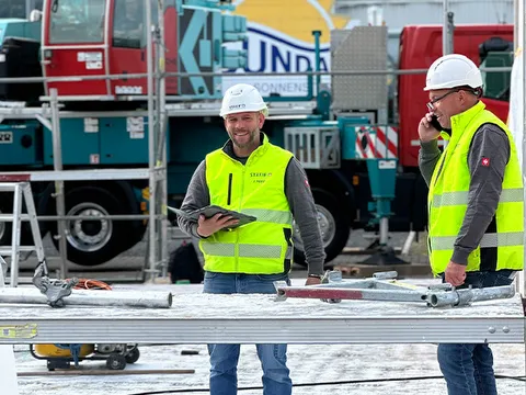 STREIF Mitarbeiter mit Schutzhelmen und Warnwesten stehen auf einer Baustelle, einer hält ein Tablet, der andere funkt.