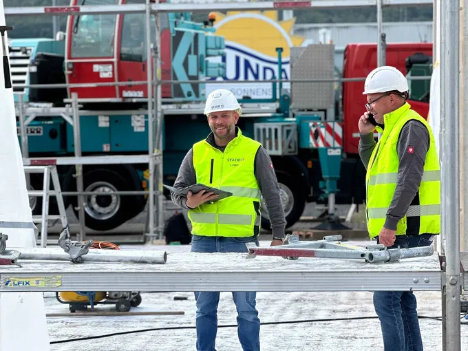 STREIF Mitarbeiter mit Schutzhelmen und Warnwesten stehen auf einer Baustelle, einer hält ein Tablet, der andere funkt.