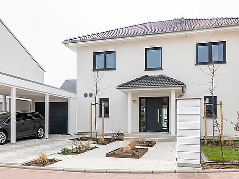 Modernes Einfamilienhaus mit hellem Putz, schwarzen Fensterrahmen und angrenzendem Carport für ein geparktes Auto