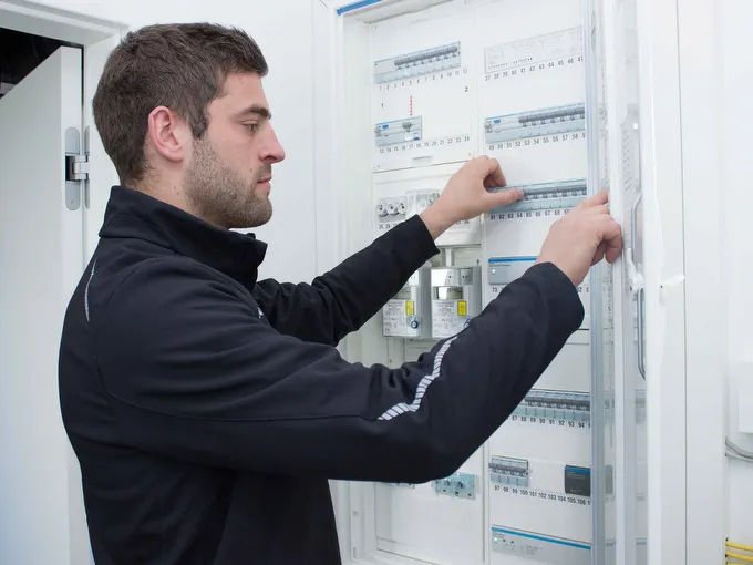 Mitarbeiter STREIF prüft Elektroverteiler mit Sicherungen in hellem Technikraum aus Seitenansicht