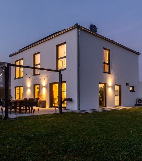 Fertighaus Flachdachhaus mit beleuchteter Fassade und großen Fenstern in der Abenddämmerung