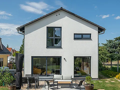 Fertighaus Einfamilienhaus zweigeschossig mit Satteldach, weißer Putzfassade, bodentiefen Fenstern und Terrasse im Garten