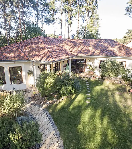 Fertighaus Bungalow Außenansicht im mediterranen Stil mit Walmdach, hell verputzter Fassade, Terrasse und Garten