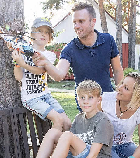 STREIF Situation Familie sitzt auf Holzterrasse im Garten vor Bäumen