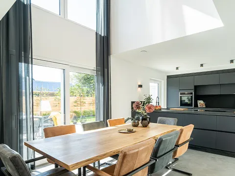 STREIF Innenraum mit offener schwarzer Küche, großem Holzesstisch und bodentiefen Fenstern im hohen Wohnraum