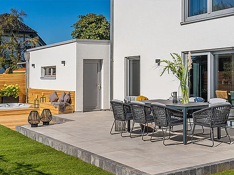 Fertighaus Terrasse mit weißer Fassade, grauen Fenstern, Sitzgruppe und Gartenbereich