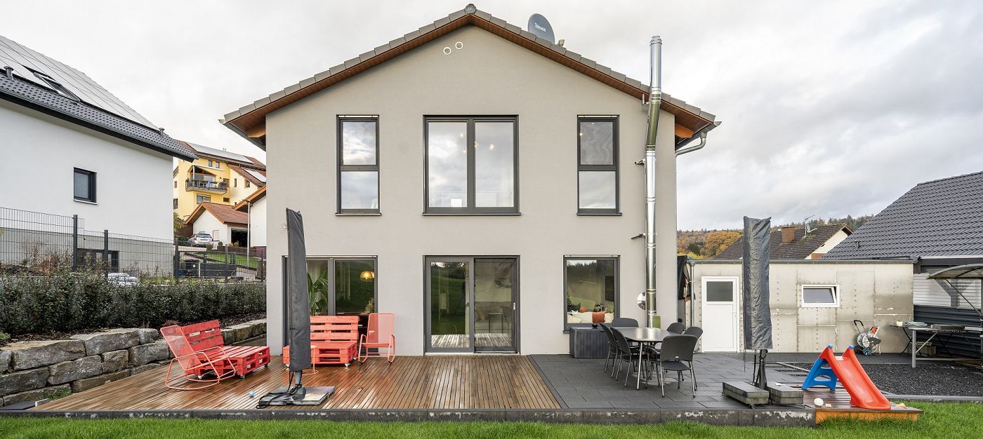 Fertighaus Einfamilienhaus Rückansicht mit Satteldach, Terrasse, Sitzmöbeln, großen Fenstern und Garten