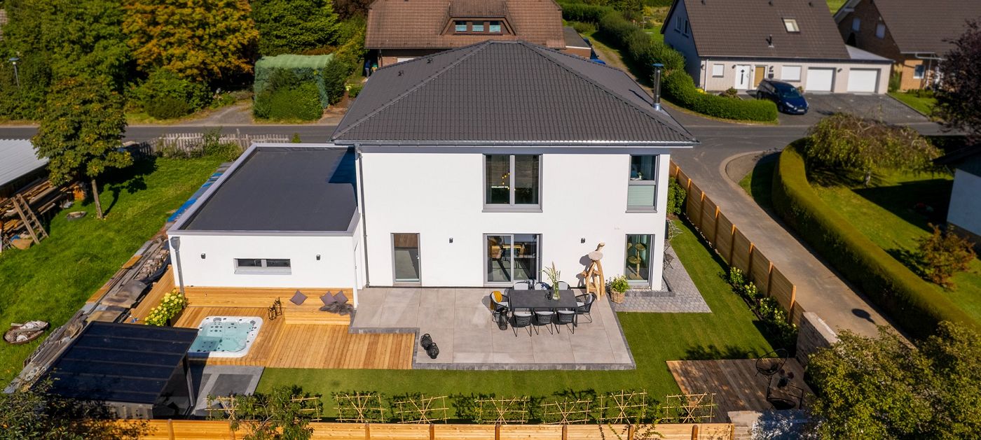 Fertighaus Stadtvilla mit Walmdach, weißer Putzfassade, großen Rechteckfenstern, Terrasse im Wohngebiet