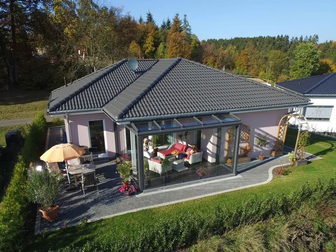 Fertighaus Bungalow mit Walmdach, verglastem Wintergarten, Terrasse und Garten in erhöhter Außenansicht