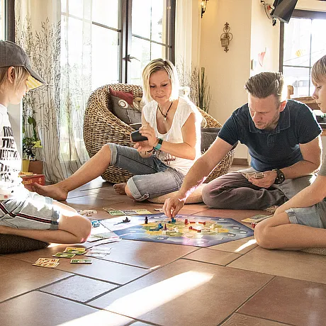 Familie spielt gemeinsam ein Brettspiel auf dem Boden eines hellen Wohnraums in einem STREIF Bungalow