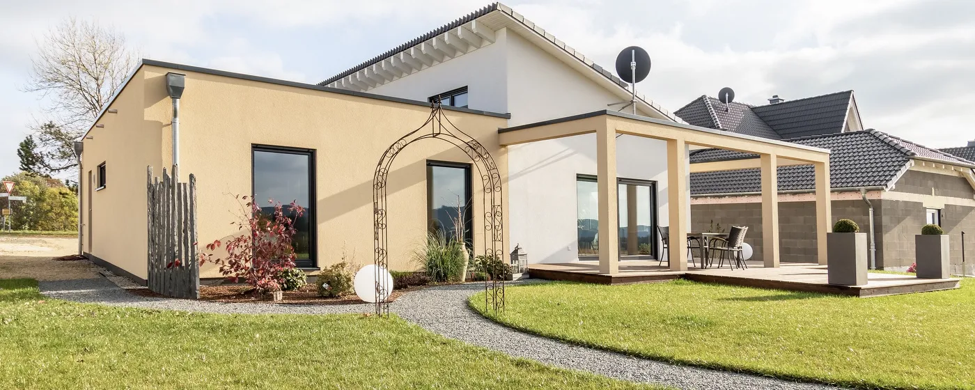Fertighaus Bungalow mit hellem Putz, Satteldach, Terrasse, bodentiefen Fenstern und Gartenanlage im Wohngebiet