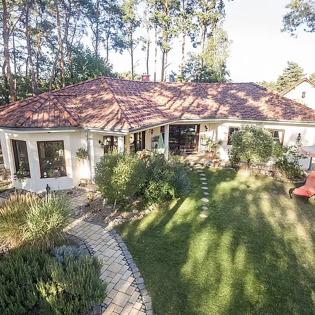 Fertighaus Bungalow Außenansicht im mediterranen Stil mit Walmdach, hell verputzter Fassade, Terrasse und Garten