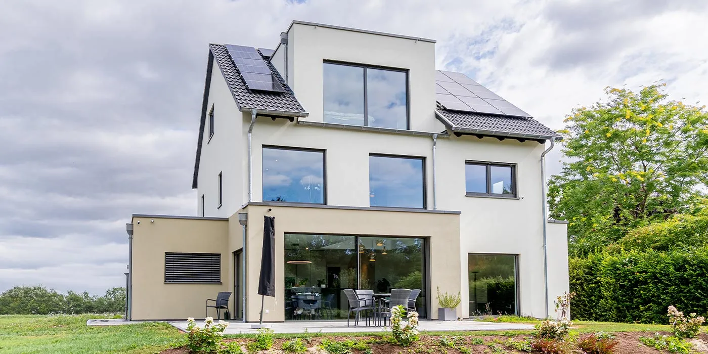 Fertighaus Einfamilienhaus mit weiß-beiger Fassade, großen Fenstern, Terrasse und Photovoltaikanlage auf dem Satteldach