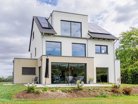 Fertighaus Einfamilienhaus mit weiß-beiger Fassade, großen Fenstern, Terrasse und Photovoltaikanlage auf dem Satteldach