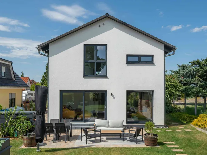 Fertighaus Einfamilienhaus zweigeschossig mit Satteldach, weißer Putzfassade, bodentiefen Fenstern und Terrasse im Garten