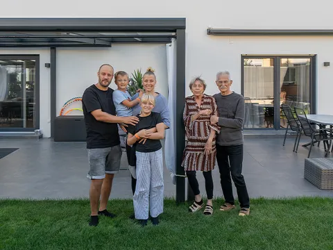 Mehrgenerationenwohnen Familie mit sechs Personen vor modernem Wohnhaus mit Terrasse und Rasenfläche.
