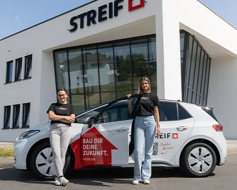 Azubis stehen am STREIF-Azubiauto vor dem Verwaltungsgebäude.