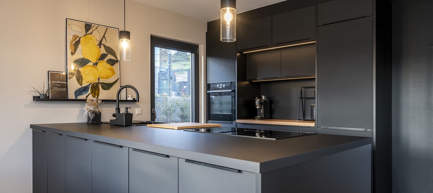 Innenraum moderne Küche mit Kochinsel, dunklen Fronten, Einbaugeräten, Pendelleuchten und Fenster