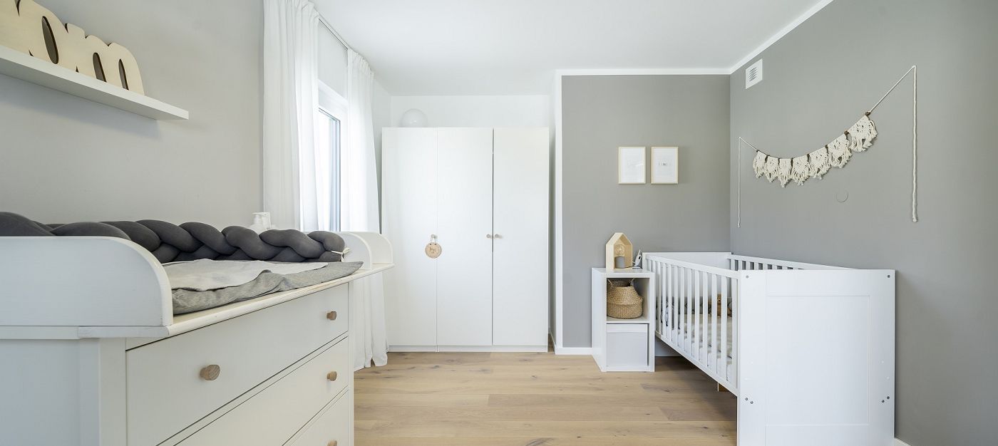 Babyzimmer mit Gitterbett, Wickelkommode, Kleiderschrank, Holzfußboden und Fenster