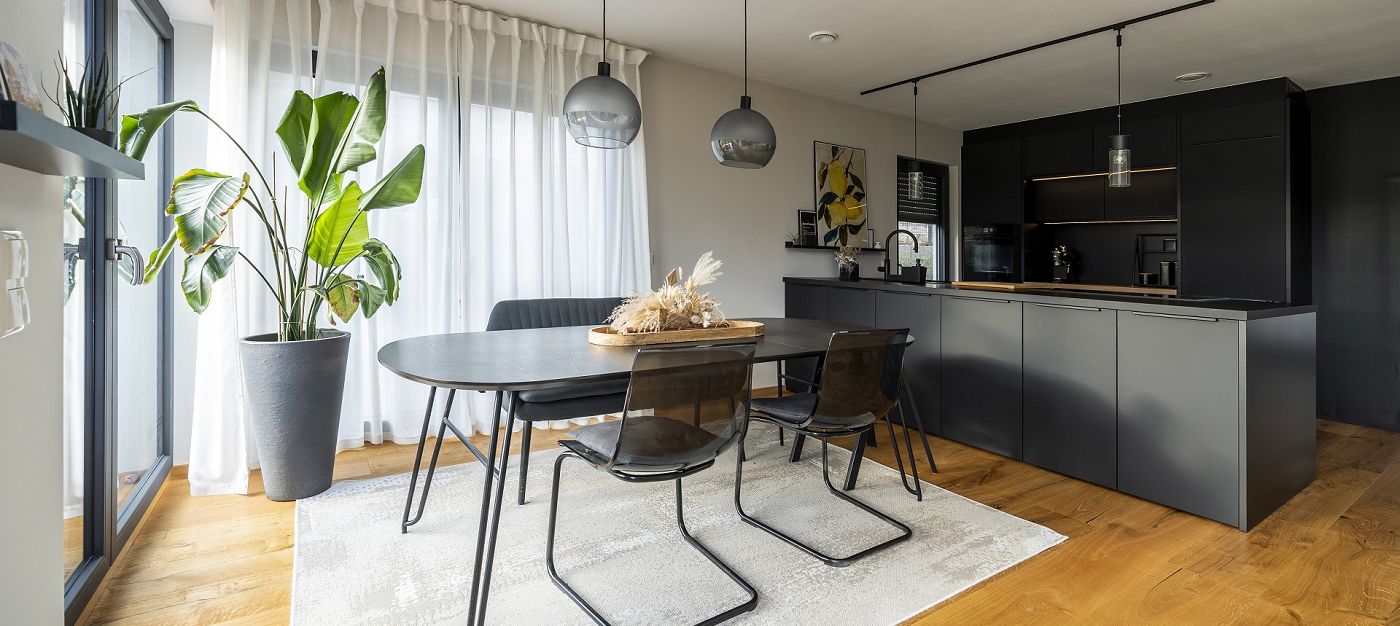 Innenraum moderner Essbereich mit rundem Tisch, schwarzen Stühlen, offener Küche und großen Fenstern