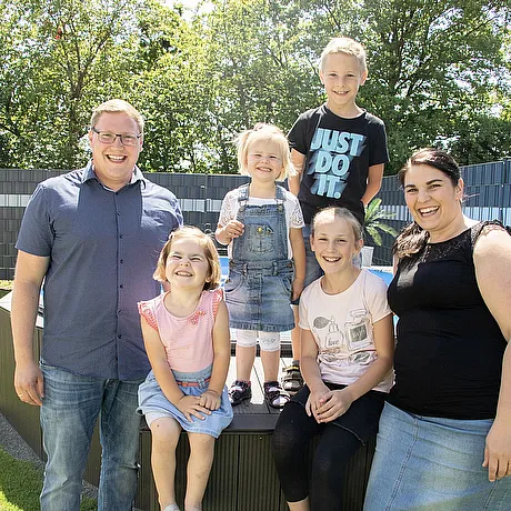 STREIF Situation Familie steht gemeinsam im Garten vor Hecke und Bäumen