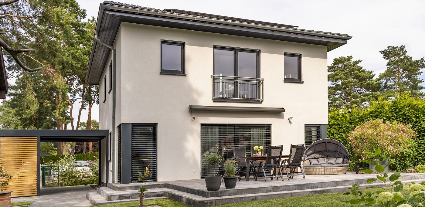 Fertighaus Stadtvilla mit Walmdach, heller Putzfassade, Balkon, bodentiefen Fenstern, Terrasse und Garten