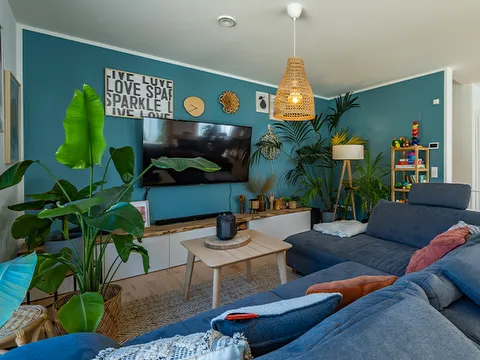 STREIF Innenraum mit blauem Ecksofa, TV-Wand, Zimmerpflanzen und heller Pendelleuchte im Wohnbereich