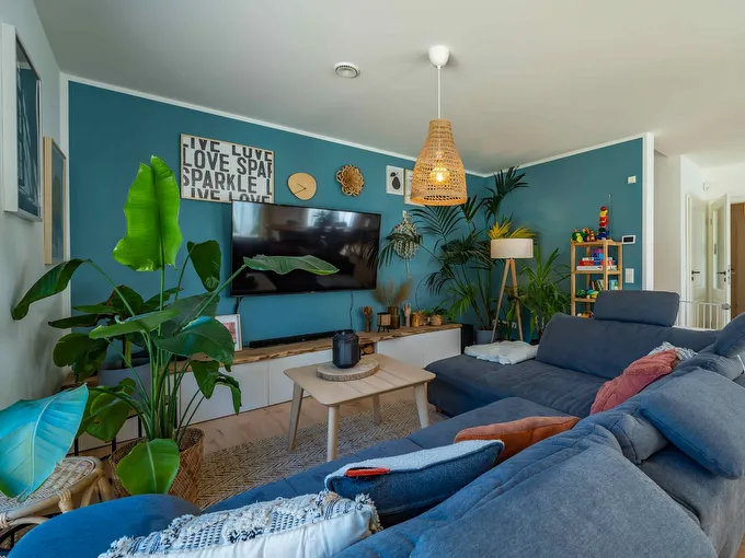 STREIF Innenraum mit blauem Ecksofa, TV-Wand, Zimmerpflanzen und heller Pendelleuchte im Wohnbereich