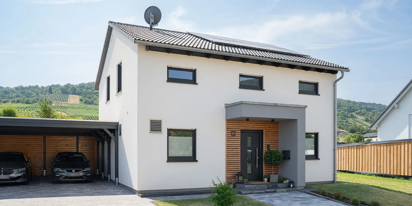 Fertighaus Einfamilienhaus mit weißer Fassade, Satteldach, Holzdetails am Eingang und Doppelcarport in Weinberglandschaft