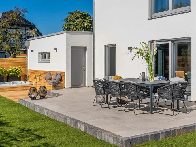 Fertighaus Terrasse mit weißer Fassade, grauen Fenstern, Sitzgruppe und Gartenbereich