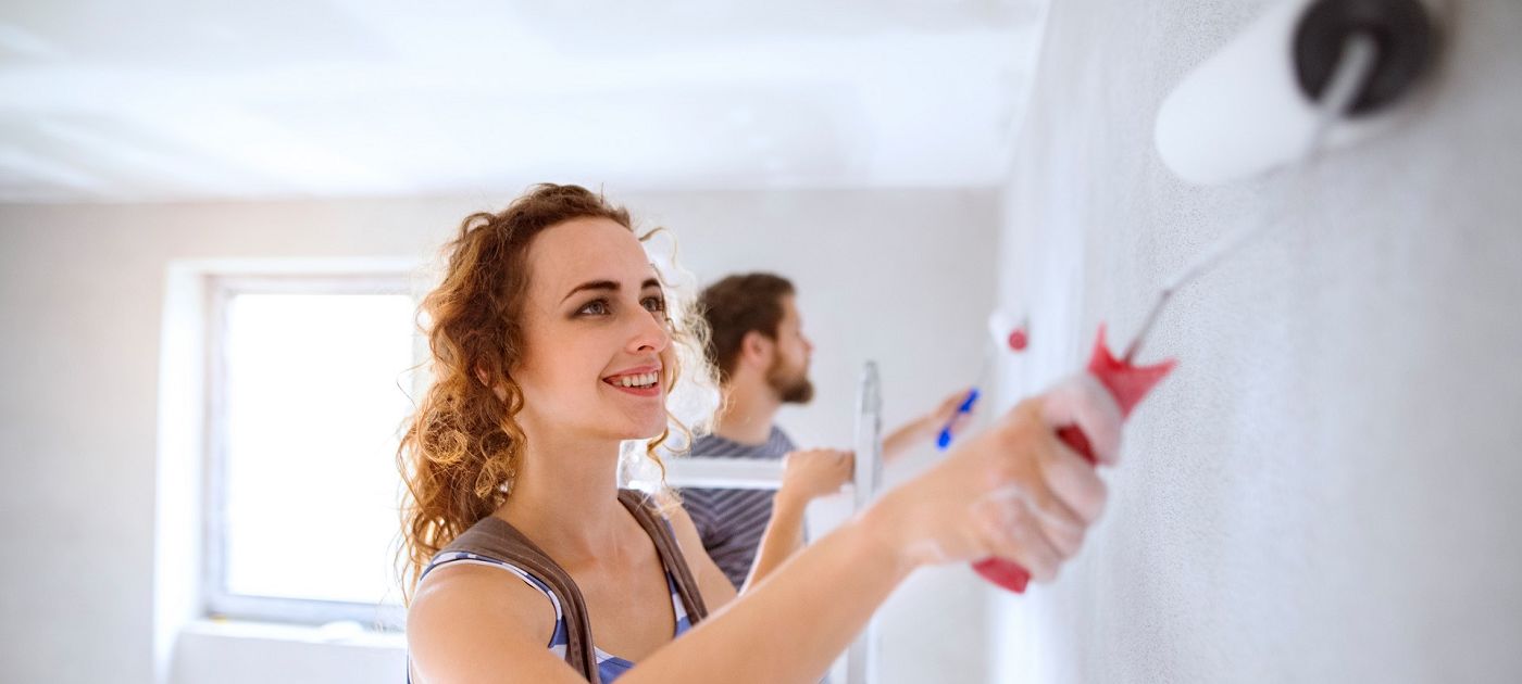 Person Renovierung Frau beim Streichen einer Innenwand mit Farbrolle, im Hintergrund weitere Person bei Arbeiten